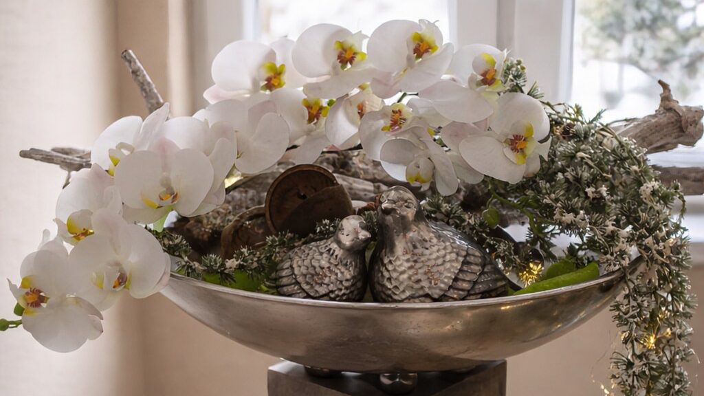 Dekosäule mit weißen Orchideen und winterlichen Elementen in einer Metallschale auf einer Säule
